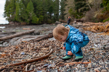 Curious toddler explores a shoreline on Vancouver Island. Dressed for the weather and engaged in outdoor free play, they collect small treasures. This highlights unstructured playand time outdoors