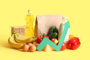 Shopping bag with food products and arrow on yellow background. Price rise concept