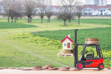 tiny home on stack coins with miniature toy forklift machine over blurred background.