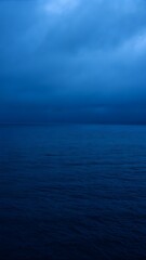 Fototapeta premium Dark blue seascape a calm ocean under a cloudy somber sky