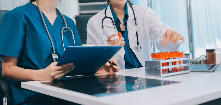 Medical team meeting analyzing blood test results in hospital laboratory. Doctors and scientists in lab coats are having a discussion about blood test result, holding test tubes and taking notes.