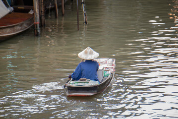 Obraz premium Local vendors paddle wooden boats filled with fresh produce through a lively floating market. This scene captures the authentic charm of traditional Thai canal life and commerce.