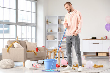 Young man mopping floor at home after party