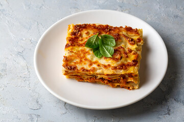 Portion of ground beef lasagna topped with melted cheese and garnished with fresh parsley served on a plate in close view for a menu