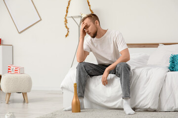 Young man with hangover sitting in bedroom after party