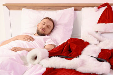 Young man with Santa costume sleeping in bedroom after Christmas party