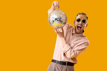Drunk young man with disco ball after Birthday party on yellow background