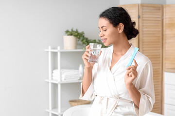 Young African-American woman taking collagen powder in bathroom