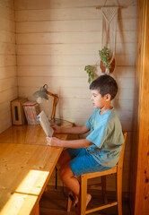 A boy is reading a book in his room at the table