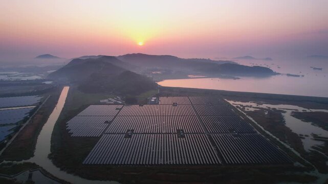 Solar power station on coastal tidal flats during sunset with mountain silhouettes and water reflections
