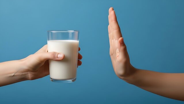Person refusing a glass of milk with a hand gesture against a blue background, concept of lactose intolerance or dairy allergy avoidance