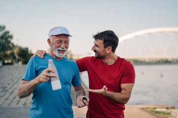 Senior man and personal trainer resting after workout by the river