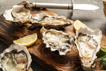 Wooden board with delicious fresh oysters and lemon on dark background, closeup