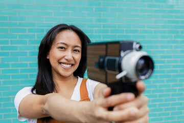 Smiling person holding retro film camera filming against turquoise wall