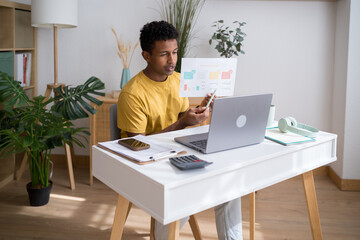 Man working from home with phone and laptop reviewing marketing presentation