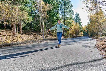 Traveler with backpack walking on road through autumn forest enjoying nature