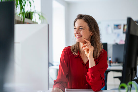 Cheerful woman with hand on chin at office