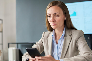 Woman in formalwear using smartphone in modern office setting