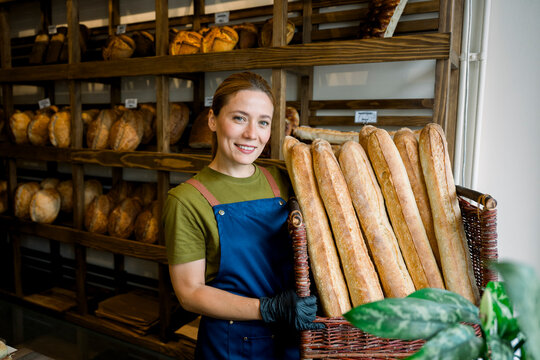 Saleswoman holding basket of bread in bakery shop smiling
