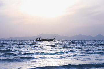 Small fishing boat on calm sea at sunset with distant island silhouette and soft pastel sky