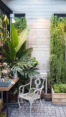 Elegant garden patio featuring a white ornate chair and lush monstera plants. Rustic outdoor living space with tropical greenery and wooden background for lifestyle design