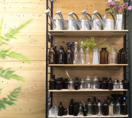 Vintage watering cans and glass apothecary bottles on a rustic wooden shelf. Sustainable lifestyle and gardening shop display with brown and clear glass containers