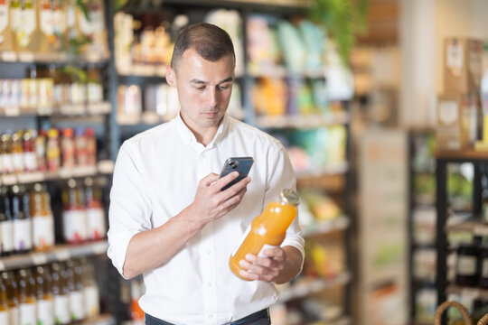 Focused male shopper scanning barcode on juice bottle with smartphone to make mobile payment in organic grocery store. Concept of technology enhancing shopping experience