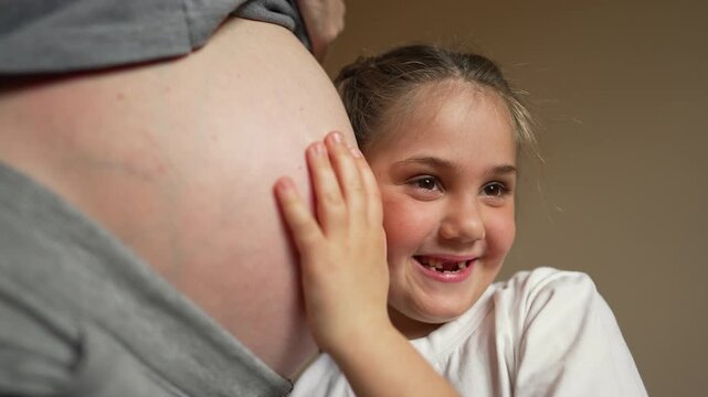 Girl presses pregnant belly gently while smiling and listening to baby movement, daughter showing love and bond with mother, child and family connection pregnancy and belly focus for baby bonding.