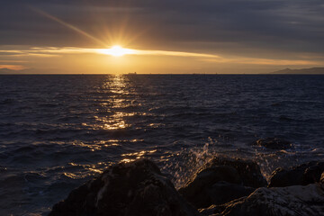 Moody sunset scene with golden light reflecting on dark Aegean Sea waves under layered clouds. Peaceful seascape near Athens, Greece, suitable for travel, nature and background use.