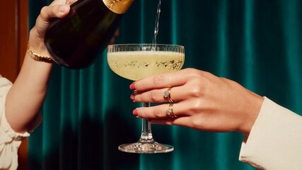 Sparkling drink is poured from bottle into elegant cocktail glass against teal curtain capturing celebration luxury party mood and festive evening lifestyle