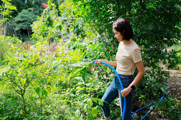 Woman watering plants with a garden hose.