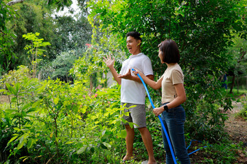 Woman and man watering plants with a garden hose.