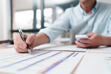 Businessman reviewing financial documents while holding a smartphone at the office desk. Concept of financial analysis, business review, accounting, and digital finance management.