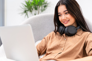 Young beautiful, stylish, happy Asian woman with headphone on neck smiling, looking at computer laptop. Digital technology, modern lifestyle, online learning, streaming services
