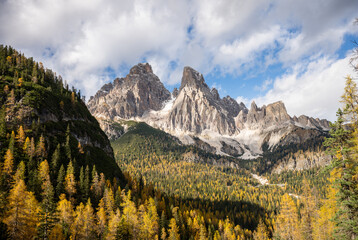 Dramatic rocky Dolomites mountain peaks above autumn forest under blue sky