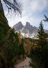 Hiking trail leading through autumn forest toward dramatic Dolomites mountain peaks