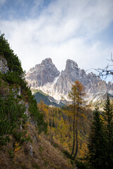 Dramatic rocky Dolomites mountain peaks above autumn forest under blue sky