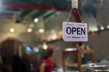 A white "Open" sign hanging on a glass door, welcoming customers into a shop with warm lighting.