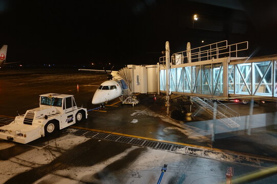 ANA turboprop plane connected to jet bridge and pushback tractor at Memanbetsu Airport at night in winter.