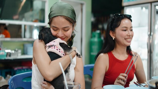 Thai friends enjoying moo krata together, woman cuddling her adorable puppy