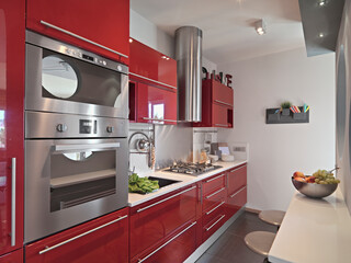 Interior view of a modern red lacquered kitchen, with built-in ovens in the foreground.