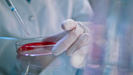 A gloved hand carefully dispenses red liquid into a test tube, symbolizing precision in medical research. The sterile lab setting underscores meticulous healthcare and biology experiments. © stockcopter