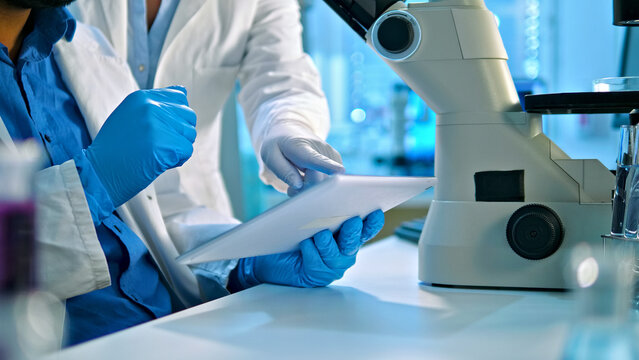 In a lab, a researcher in a white coat and blue gloves examines a document beside a microscope, highlighting precision and the critical role of documentation in medical research.
