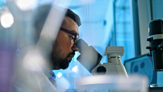 A researcher examines a specimen under a microscope in a lab, surrounded by scientific equipment. The setting emphasizes precision and innovation in healthcare and biology.