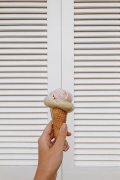 Summer Bliss: Close-Up of a Hand Holding a Flavorful Ice Cream Cone Against a White Shutters