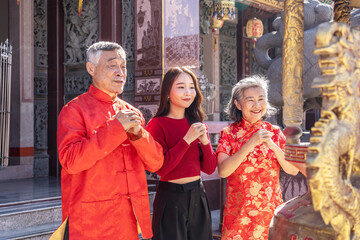 Naklejka premium An Asian family father mother and young daughter dressed in bright cheongsams stands together, hands clasped in prayer, in a vibrant Chinese temple during Lunar New Year celebrations