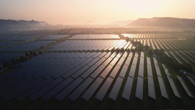 Large-scale photovoltaic power station array at sunrise with reflective solar panels and distant hills
