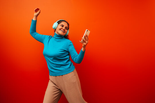 Curly woman dancing with headphones and mobile phone by orange wall