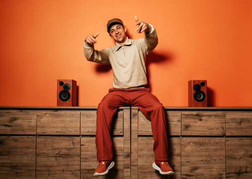 Smiling man dancing and gesturing with music speakers in orange room