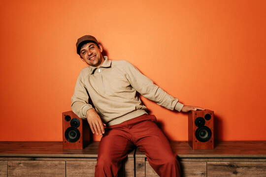 Smiling man in casual clothing with vintage speakers on orange background